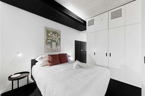 Een moderne slaapkamer met een bed, een bureau, een stoel, een kledingkast en een schilderij aan de muur.