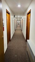 Un largo pasillo de hotel, estrecho, con puertas de madera a ambos lados, suelo cubierto de alfombra y una lámpara en el techo.