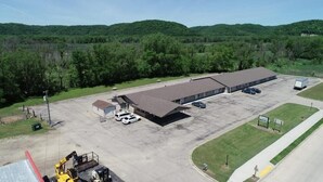 A large industrial building with a flat roof, a parking lot, and a small green area with a sign. - SANDS MOTEL (Boscobel)