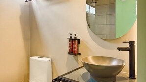 Een moderne badkamer met een toilet, een glazen wastafel met kom, een handdoekhouder en een spiegel.