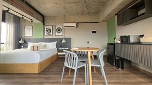 Een moderne hotelkamer met een bed, een eettafel met stoelen, een keukenhoek en een groot raam.
