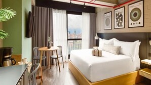 Hotelkamer met een bed, een bureau, een stoel, een koffiezetapparaat en uitzicht op de stad.