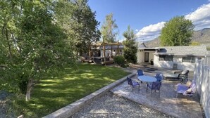 Ein Garten mit Terrasse, Sitzgelegenheiten im Freien, einer Pergola und einem Haus.