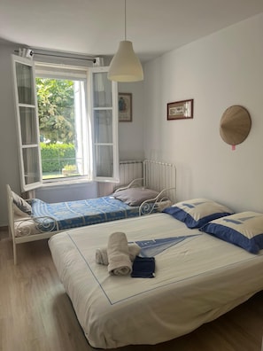Une chambre avec deux lits, une fenĂȘtre avec des rideaux, un luminaire suspendu et un radiateur.