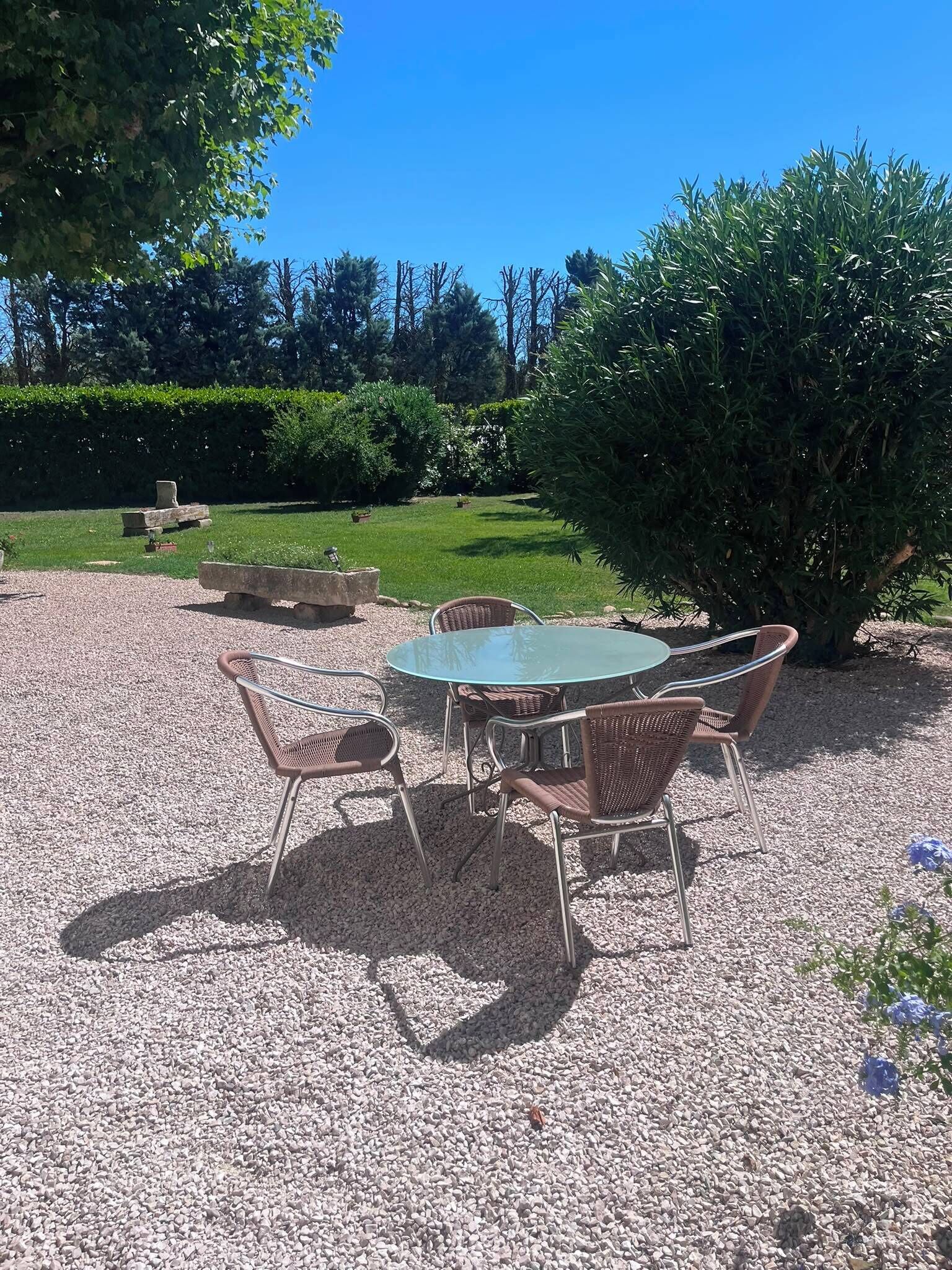 Ein Sitzbereich im Freien mit einem runden Tisch und Korbstühlen, umgeben von Kies.