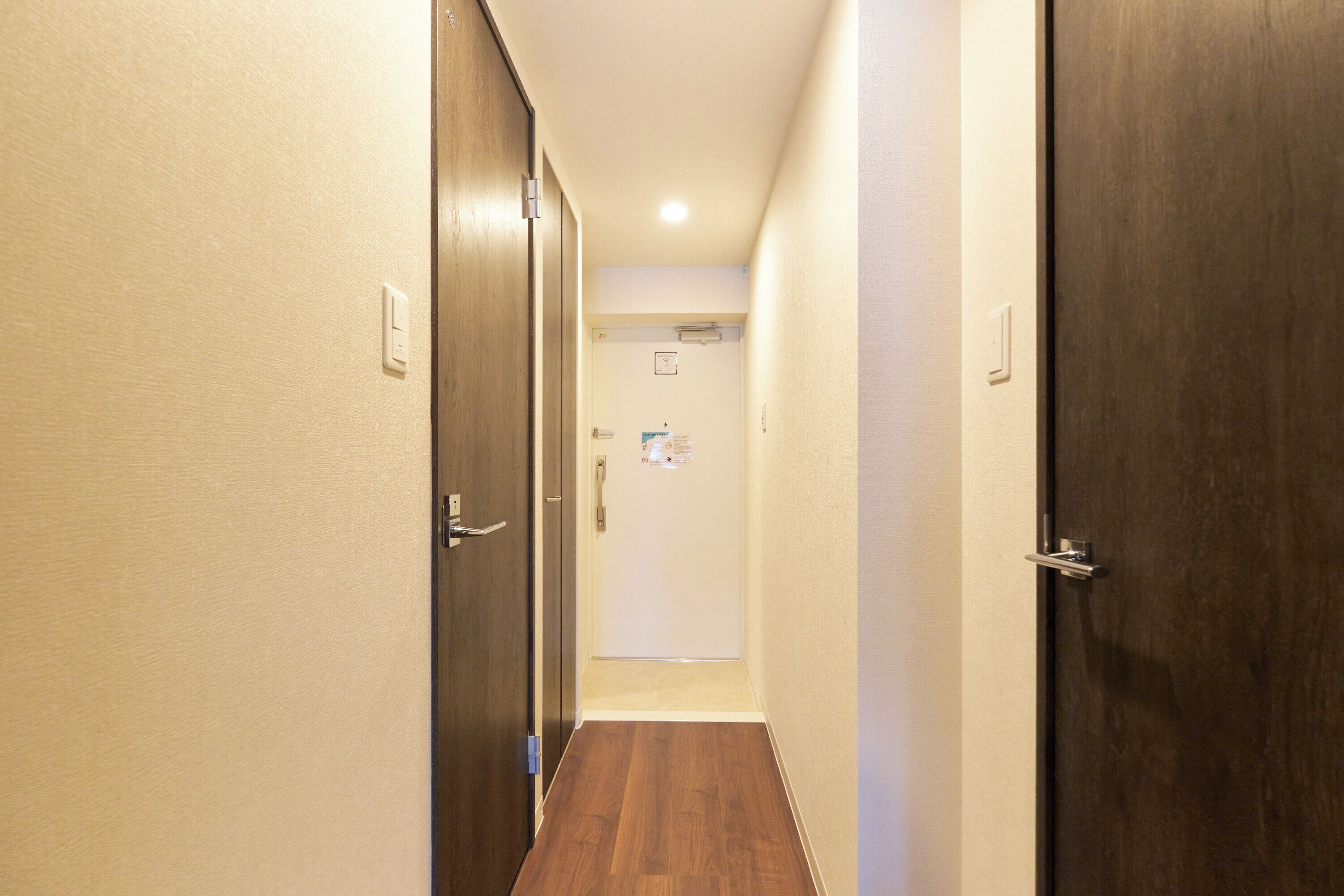 A hallway with wooden doors, a light switch, and a door with a notice.