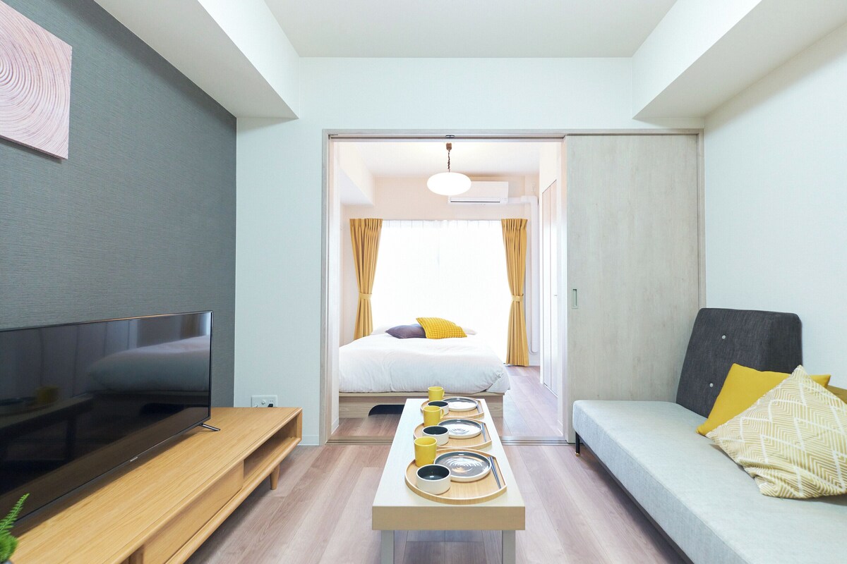 Una habitación moderna con televisión de pantalla plana, una mesa de comedor con platos y tazas, un sofá y una cama con cortinas.
