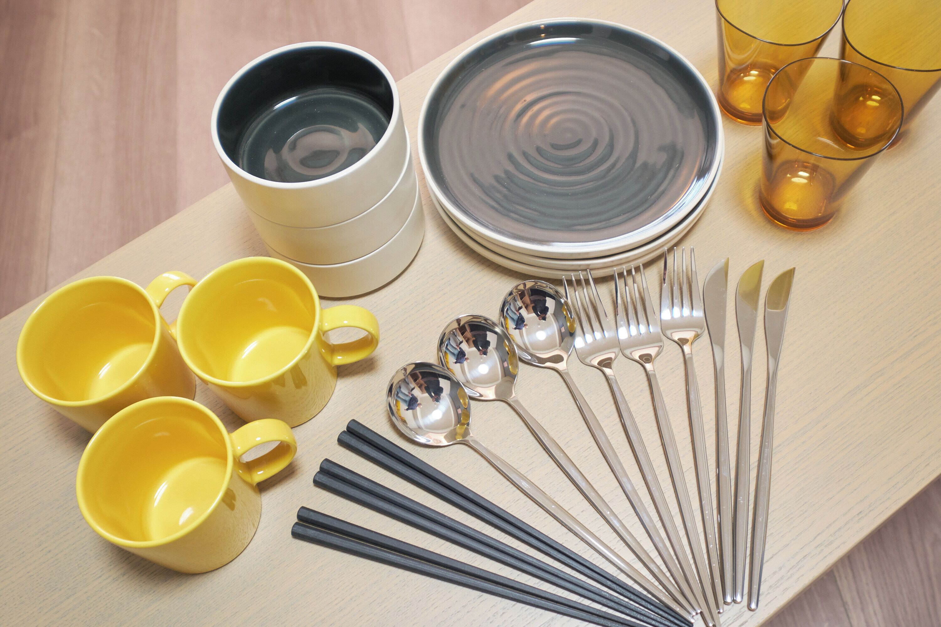 Un service de table comprenant des tasses, des assiettes, des couverts et des verres, posé sur une table en bois.