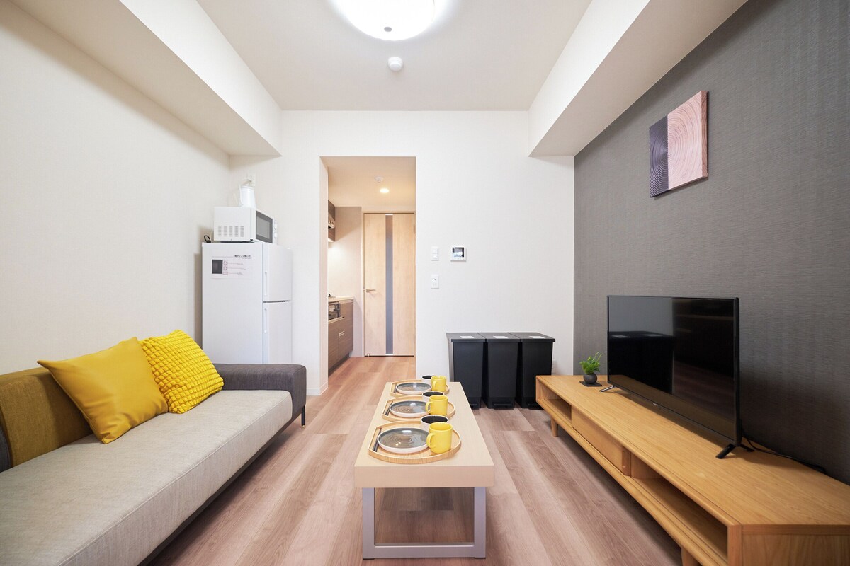A modern living room with a sofa, coffee table, TV, and a kitchen area in the background.