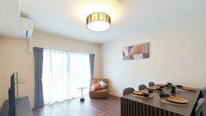 A modern living room with a flat-screen TV, a dining area with a table set for four, and a sofa with cushions. - AQUA RESIDENCE Sangenjaya by Tranova 2 (Setagaya)