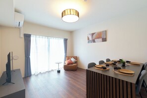 A modern living room with a flat-screen TV, a dining area with a table set for four, and a sofa with cushions. - AQUA RESIDENCE Sangenjaya by Tranova 2 (Setagaya)