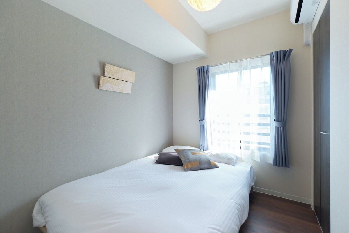 Un dormitorio con cama, una ventana con cortinas, aire acondicionado instalado en la pared y una lámpara.