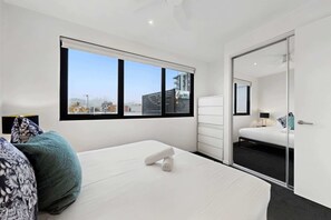 Ein modernes Hotelzimmer mit großem Fenster, einem Bett, einem Schminktisch und einem Spiegel.