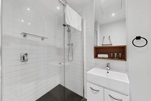 Un bagno moderno con doccia a vetro, un lavandino bianco e uno scaffale in legno con articoli da toilette.