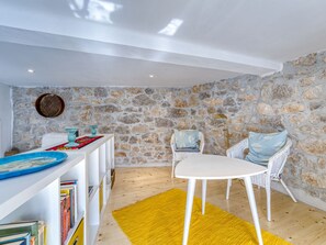 Une pièce avec un mur en pierre, une table blanche, un tapis jaune et des chaises en osier.
