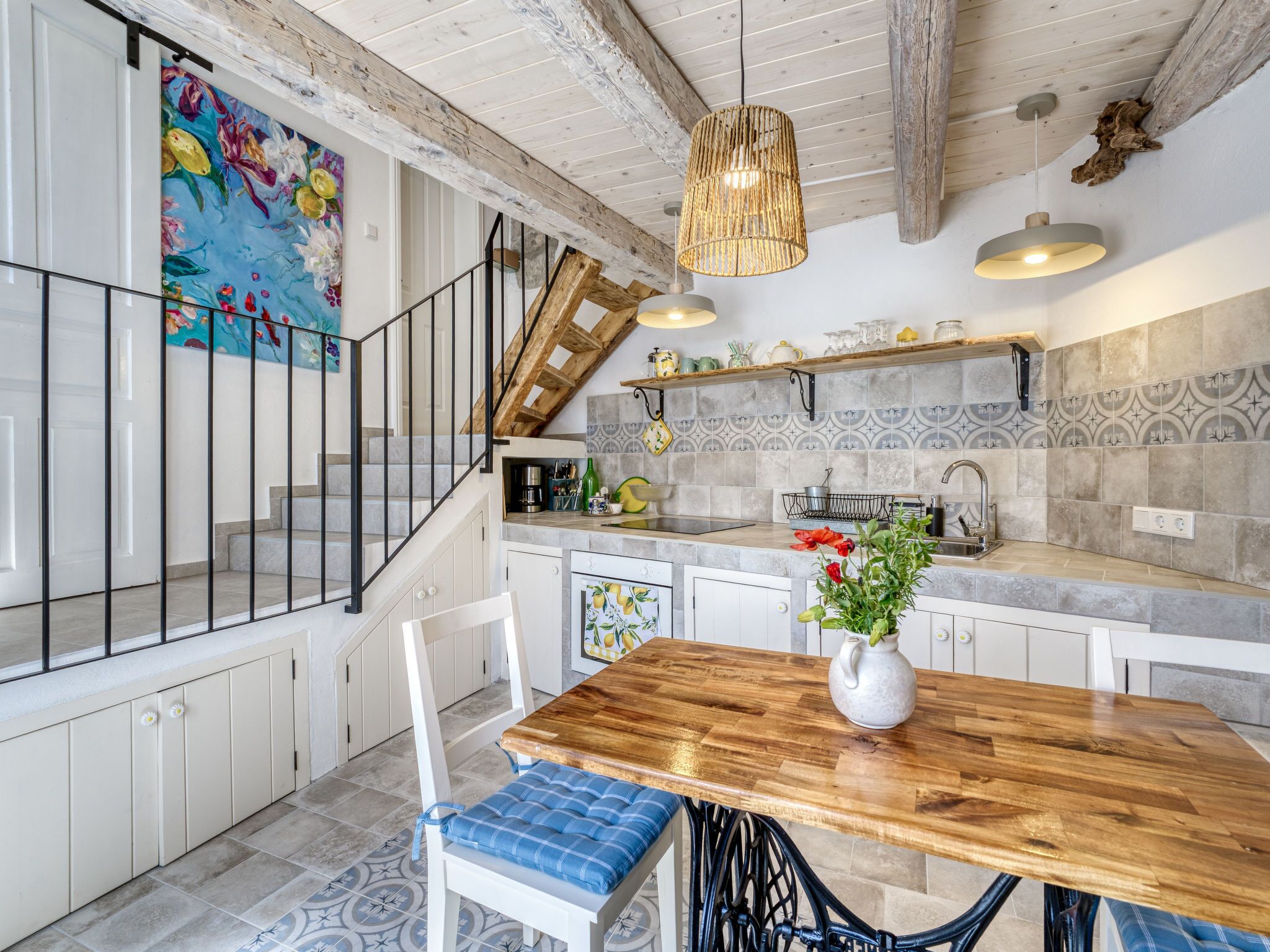 A kitchen with a wooden table, a hanging light fixture, and a staircase.