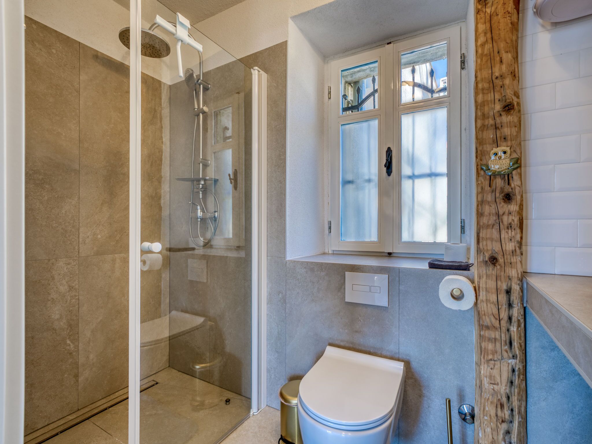 Ein Badezimmer mit einer gläsernen Duschkabine, einer Toilette und einem Fenster mit Milchglas.