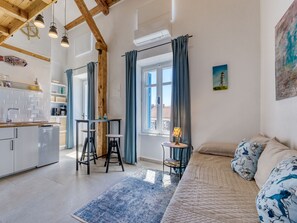 A modern kitchen with white cabinets, a wooden ceiling, and pendant lights. There is a dining area with a table and chairs, and a large window with curtains. - Passion by Interhome (Krk/Malinska)