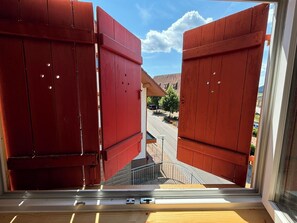 Ein Fenster mit roten Fensterläden, Blick auf eine Straße und ein klarer Himmel.