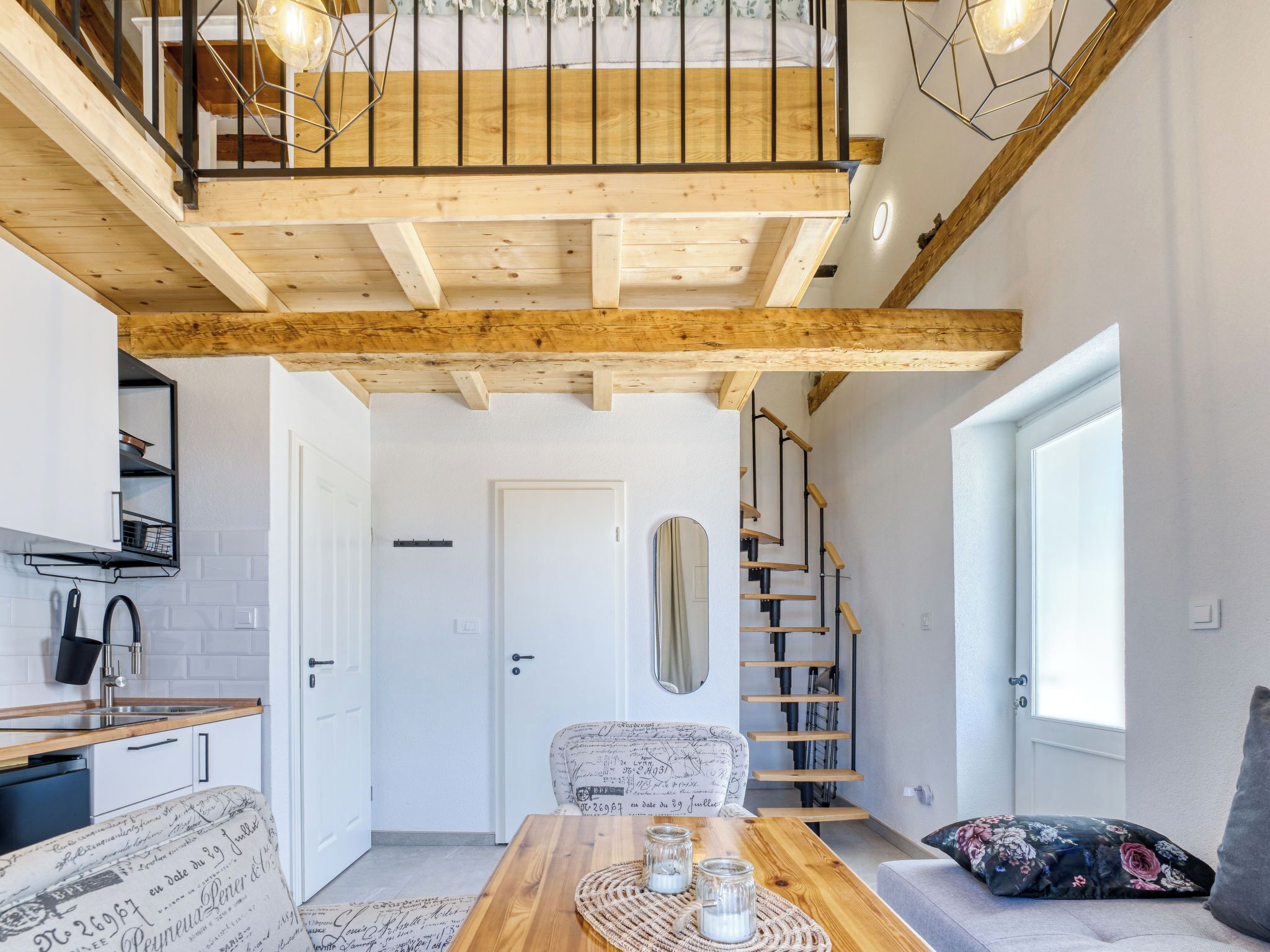Ein modernes Interieur mit einer Holztreppe, einem Essbereich mit Tisch und Stühlen, einer Küche mit Spüle und Schränken sowie einem großen Fenster.
