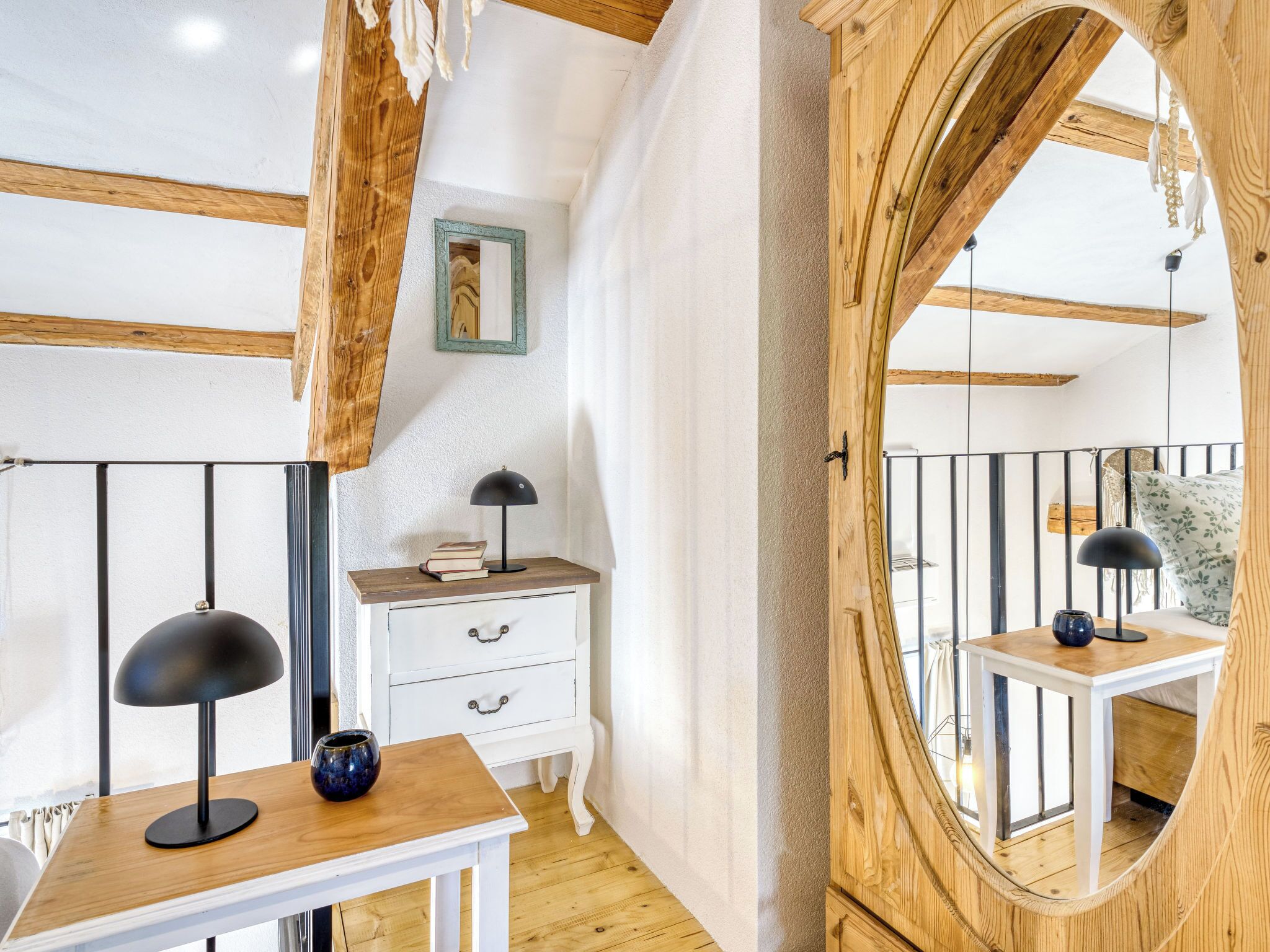 A room with a wooden ceiling, a white dresser, a mirror, and a small table with a lamp.