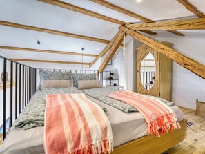 A bedroom with a sloped ceiling, a bed with floral bedding, a striped blanket, and a wooden door. - Passion by Interhome (Krk/Malinska)