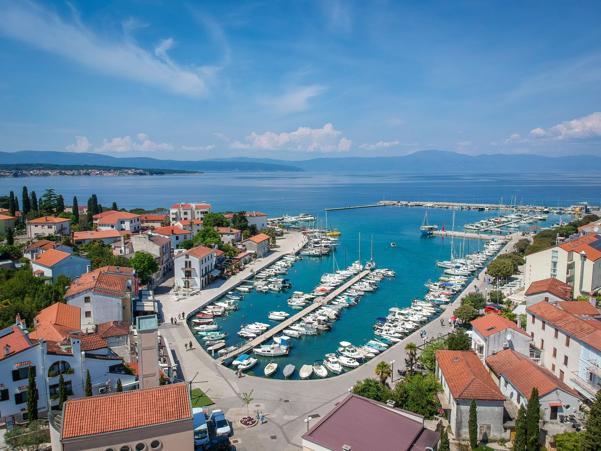 A marina with boats docked, surrounded by buildings with red-tiled roofs.