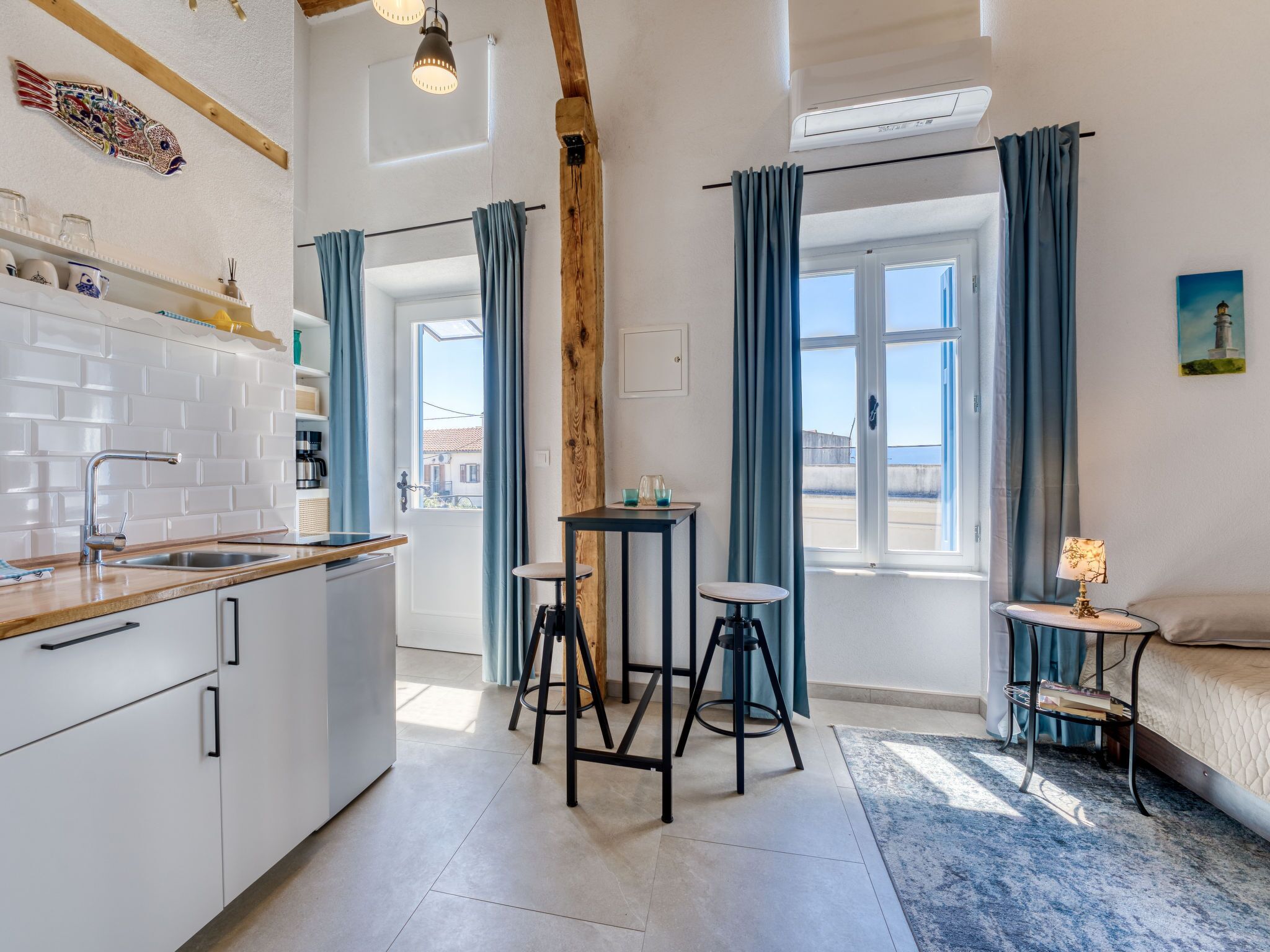 A compact kitchen with a sink, a wooden beam ceiling, and a view through a door to the outside.