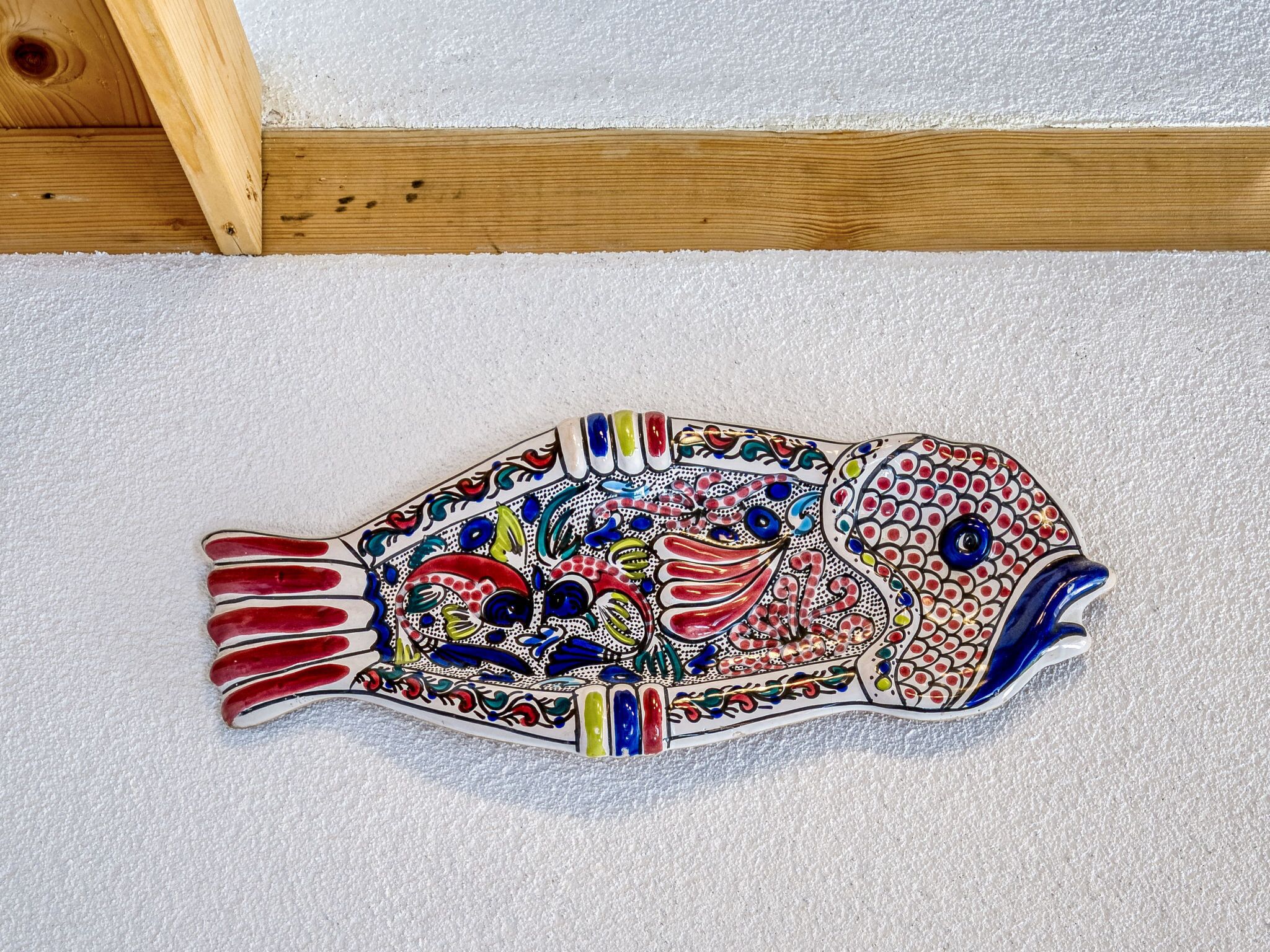 Ein farbenfrohes, fischförmiges Dekorationsobjekt auf einer weißen, strukturierten Oberfläche.