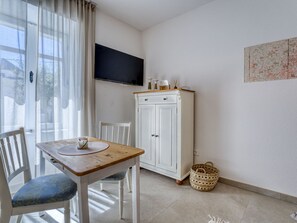 A room with a wooden table, a white cabinet, a television mounted on the wall, and a wicker basket on the floor. - Passion by Interhome (Krk/Malinska)