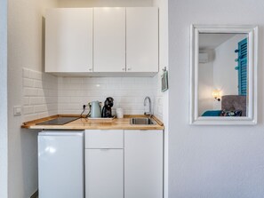 A compact kitchen with white cabinets, a sink, a coffee maker, and a small refrigerator. - Passion by Interhome (Krk/Malinska)