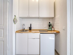 Eine kompakte Küche mit weißen Schränken, einem Edelstahl-Spülbecken, einer Kaffeemaschine und einem kleinen Geschirrspüler.