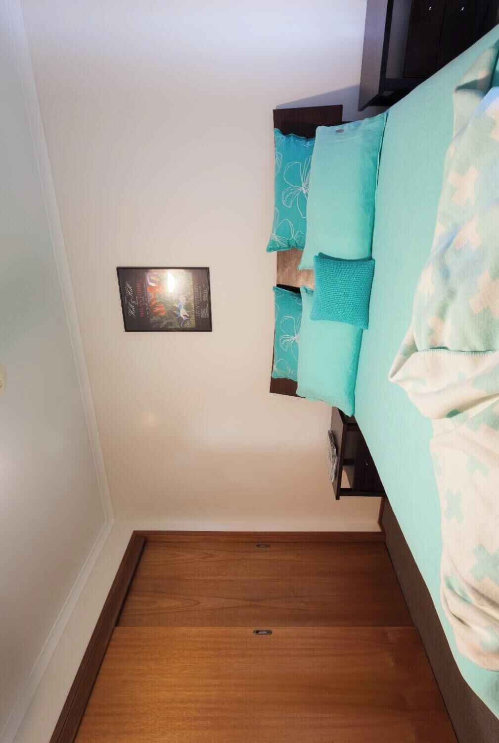 Une chambre à coucher avec un lit, une table de chevet, un tableau accroché au mur et un plancher en bois.