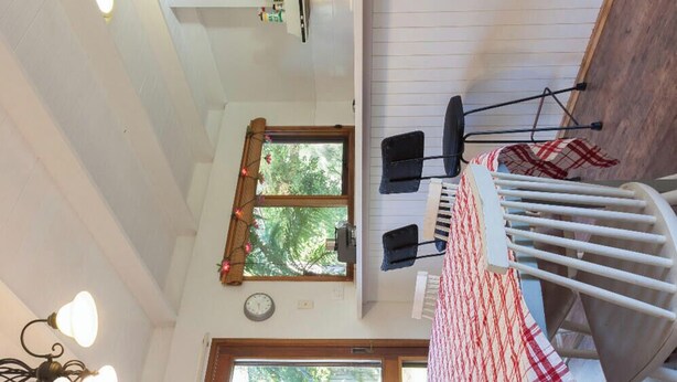A high-ceilinged room with a dining area, a window with a view of trees, and a ceiling light fixture. - All seasons for families
House on the hill 
NOW WITH  nbn, wi-fi and FOXTEL (Rosebud)