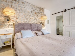Ein Schlafzimmer mit Steinwand, einem Bett mit einer gesteppten Kopfteil, Nachttischen und einem Kleiderschrank.