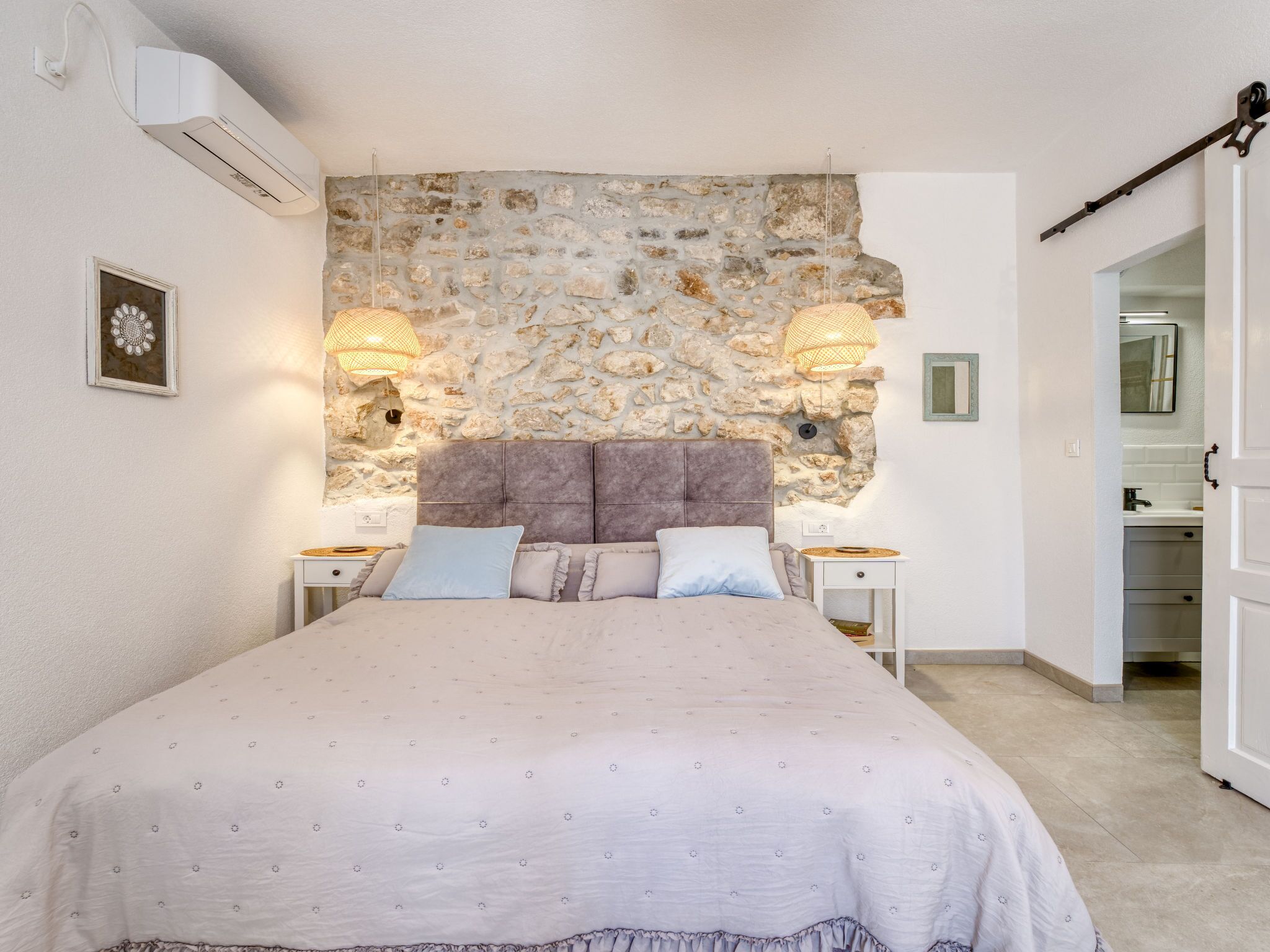 A bedroom with a stone wall, a bed with a headboard, bedside tables, and a hanging light fixture.