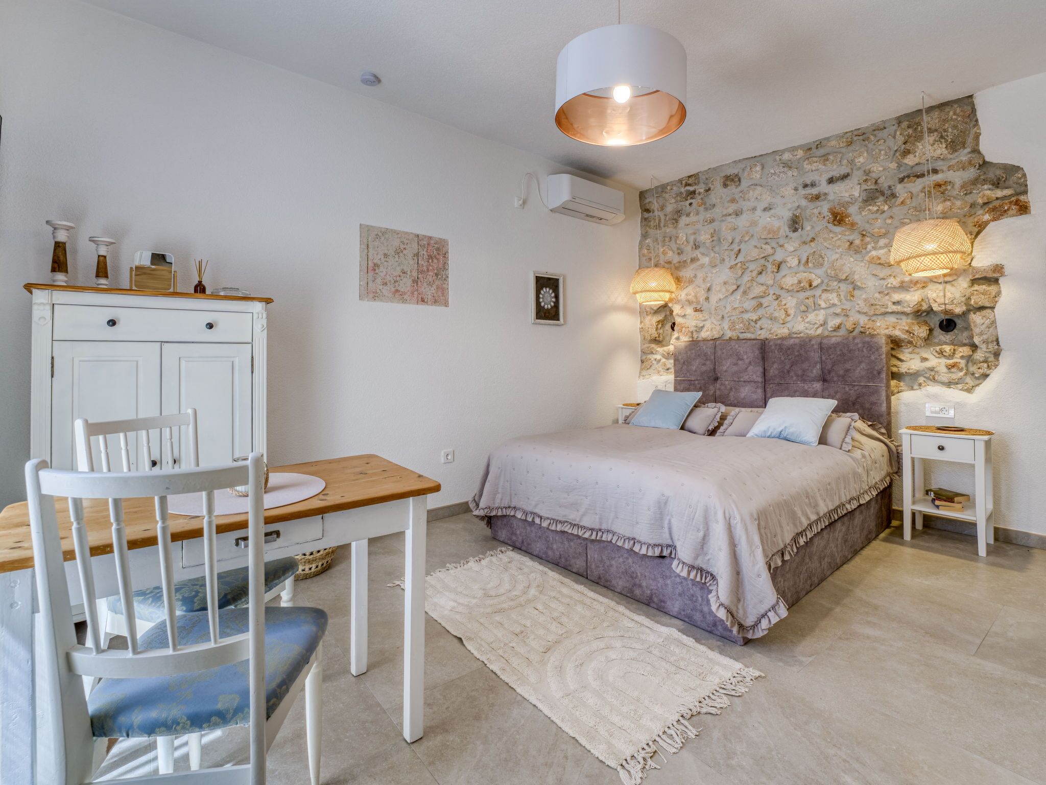 Un dormitorio con pared de piedra, una cama con cabecera, un escritorio con silla y una mesita de noche pequeña.