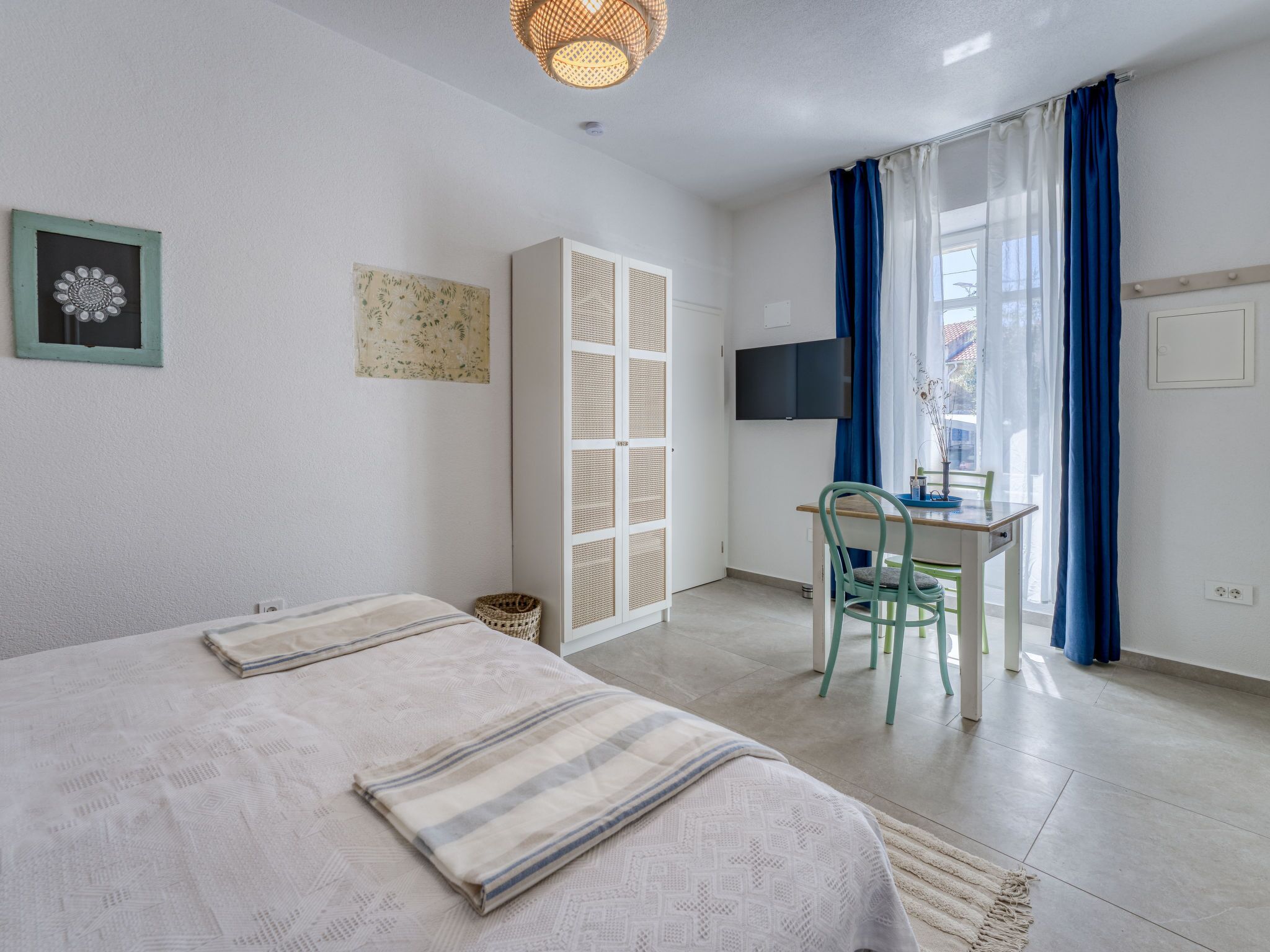 A room with two beds, a desk, a chair, a television, and a window with curtains.