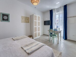 Une chambre avec deux lits, un bureau, une chaise, une télévision et une fenêtre avec des rideaux.