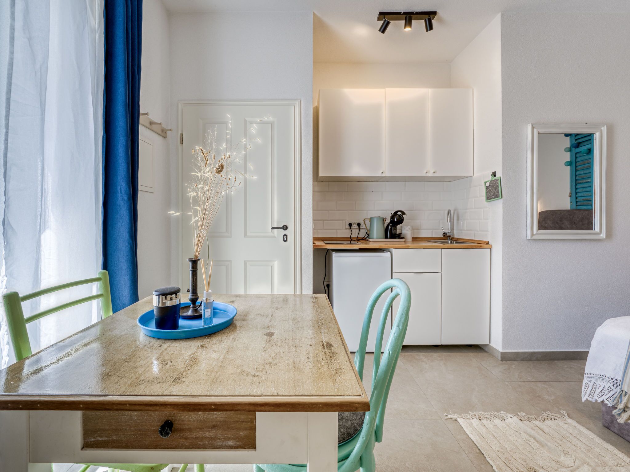 Ein Essbereich mit Holztisch, Stühlen, einer Vase mit Trockenpflanzen und einer Küche im Hintergrund.