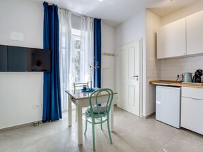Eine kompakte Küche mit Esstisch, Stühlen, einem kleinen Kühlschrank und einem an der Wand befestigten Fernseher.