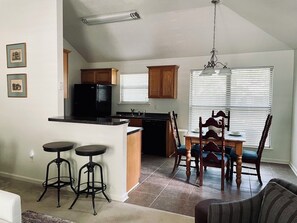A kitchen with a refrigerator, a dining table with chairs, a bar stool, and a chandelier. - Charming 3-bedroom Monthly Rental Home in Mandeville (Mandeville)