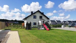 A playground with a slide and climbing net, a brick pathway, and a building in the background. - Two-story Holiday Homes With Terraces (Mielno)