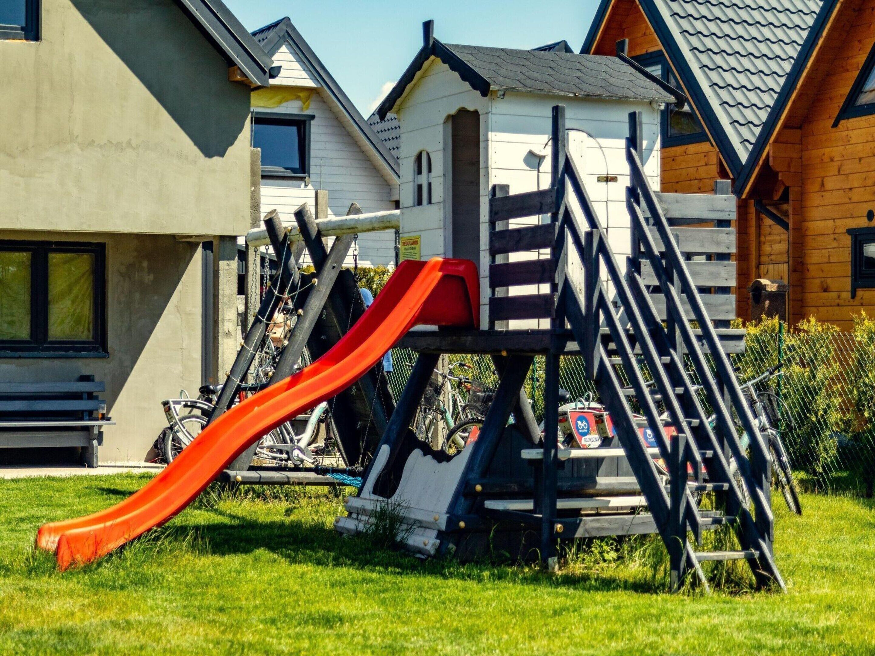 Un terrain de jeux équipé d’un toboggan et de structures d’escalade, entouré de maisons présentant différents styles architecturaux.