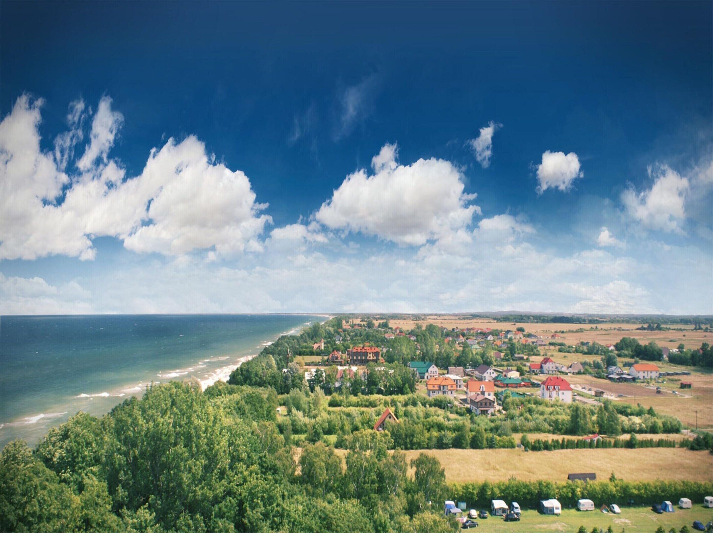 Une ville côtière avec des maisons et de la verdure, une plage et un ciel dégagé.