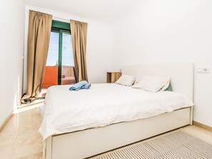 Ein Schlafzimmer mit Bett, Vorhängen, einem Nachttisch und Blick nach draußen.