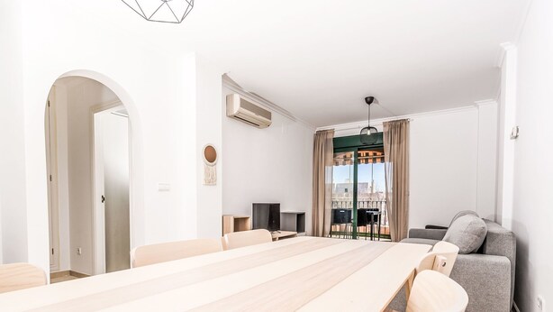 Een moderne woonkamer met een lange houten eettafel, een grijze bank en een balkon met uitzicht.