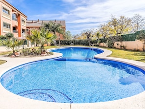 A swimming pool with a tiled edge, surrounded by a landscaped garden with palm trees and a building in the background. - Jardines del Rio by Interhome (Jávea)