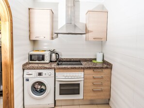 A compact kitchen with a washing machine, microwave, kettle, and oven. - Jardines del Rio by Interhome (Jávea)