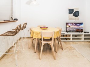 Un coin repas comprenant une table ronde, des chaises, un saladier, un téléviseur et une tapisserie murale.